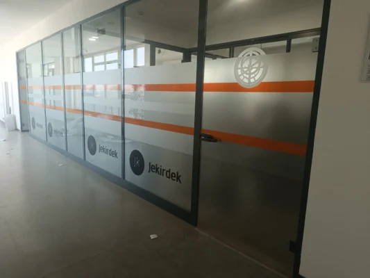 İstanbul'daki modern bir ofis bölme camına uygulanmış, üzerinde renkli ve özel tasarım desenler bulunan kesimli dekoratif kumlama cam filmi. Ofis cam giydirme sanatı..